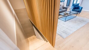 A modern staircase with wooden paneling, a glass coffee table, and a blue armchair in a contemporary living room. - Modern. Gemütlich. Zentral. - Objekt-id: Ilw/04 - Inselliebe Westerland (Sylt)