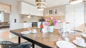 A modern kitchen with white cabinets, a wooden dining table, and pendant lights. - Modern. Gemütlich. Zentral. - Objekt-id: Ilw/04 - Inselliebe Westerland (Sylt)