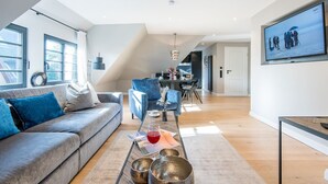 Ein modernes Wohnzimmer mit grauem Sofa, blauen Kissen, einem Couchtisch mit dekorativen Schalen sowie einem Essbereich mit schwarzem Stuhl und Tisch.