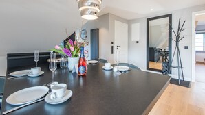 Ein moderner Essbereich mit einem dunklen Tisch, gedeckt für vier Personen, einer dekorativen Vase mit Blumen und einer Flasche Champagner.