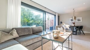 A modern living room with a grey sofa, a glass coffee table, and a dining area with a table and chairs.