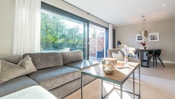 Ein modernes Wohnzimmer mit grauem Sofa, einem Glastisch und einem Essbereich mit Tisch und Stühlen.