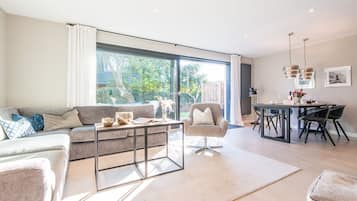 Ein modernes Wohnzimmer mit einer Couch, einem Sessel, einem Couchtisch und einem Essbereich mit Stühlen und einem Tisch.