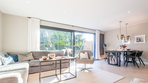 A modern living room with a sofa, armchair, coffee table, and dining area with chairs and a table.
