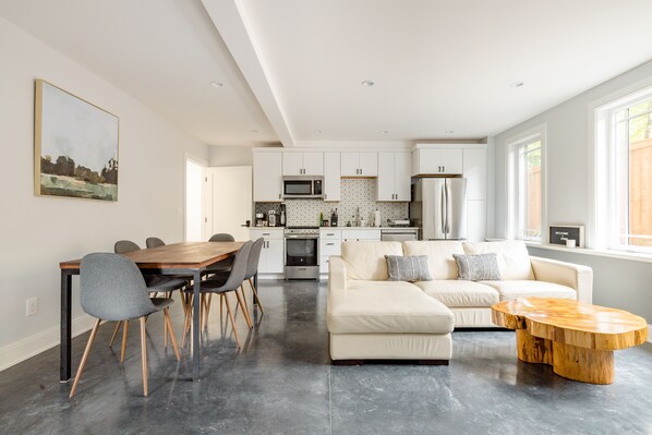 A modern kitchen with white cabinets, a dining area with a wooden table and chairs, and a living area with a sofa and coffee table.
