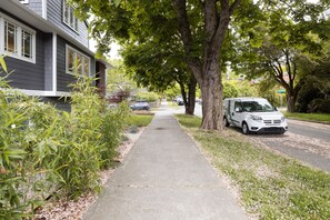 A residential street with a sidewalk, a house with a garage, and a parked car.