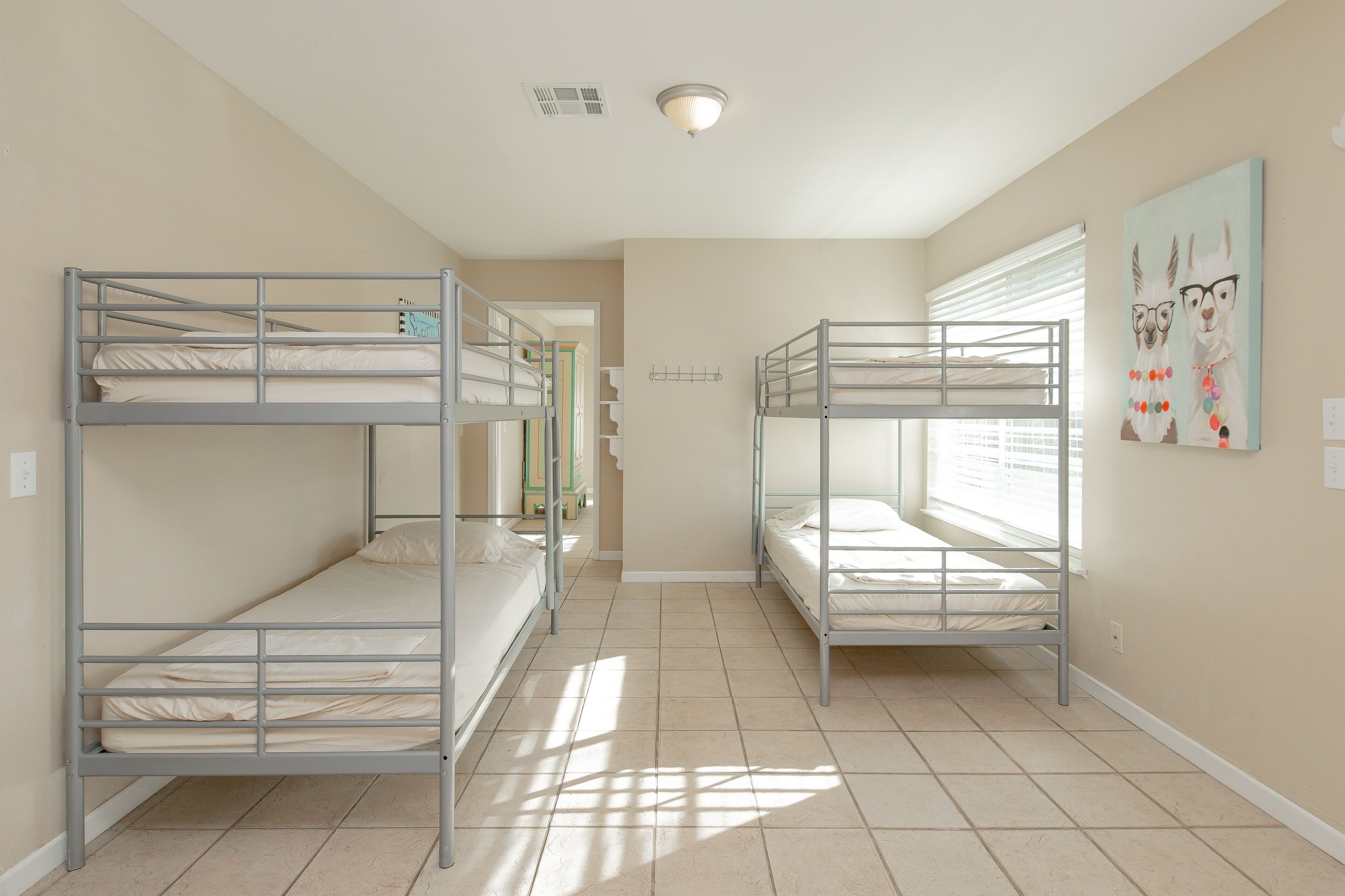 A room with bunk beds, a window with blinds, and a wall-mounted light fixture.