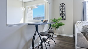 Een moderne keuken met een groot raam, een eettafel met krukken en een decoratief wandobject.