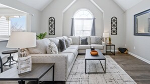 Een moderne woonkamer met een hoge plafond, een groot raam en een comfortabele hoekbank.
