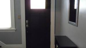 Une porte sombre, avec un luminaire au-dessus, un petit banc et un miroir accroché au mur.