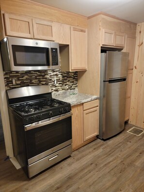A kitchen with wooden cabinets, a stainless steel stove, a microwave, and a refrigerator. - 8 min from downtown, 13 min from Airport (Carnegie)