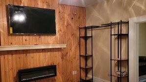 Une chambre avec un ventilateur de plafond, un téléviseur fixé au mur, une armoire en bois et un lit.