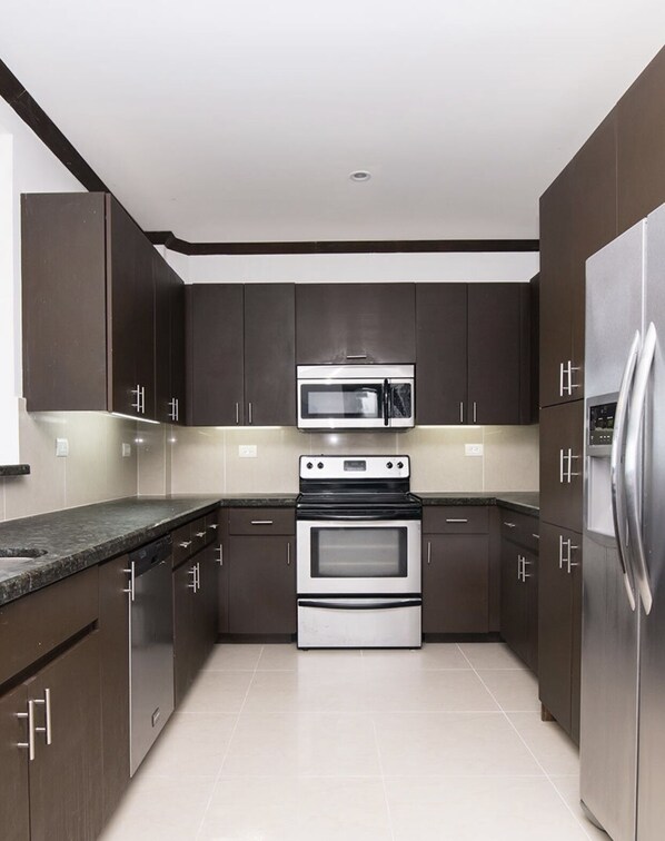 A modern kitchen with dark cabinetry, a stainless steel refrigerator, a microwave, and a double oven.