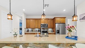 A kitchen with wooden cabinets, a stainless steel refrigerator, a microwave, and a large island with bar stools.
