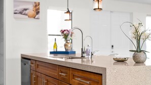 A modern kitchen with wooden cabinets, a granite countertop, pendant lighting, and a backsplash.