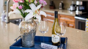 A kitchen counter with a vase of flowers, a bottle of wine, and two glasses on a blue tray.