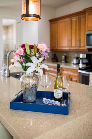 Una encimera de cocina con un jarrón de flores, una botella de vino y dos copas sobre una bandeja azul.
