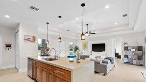 A modern kitchen with a large island, wooden cabinets, and pendant lighting.