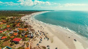 An aerial view of a beach with a row of houses along the shore, a sandy beach, and a clear blue sky. - Premium GAV Resort SMART AP 616 (Salinópolis)