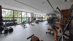 A gym with various exercise equipment, large windows, and a view of palm trees outside.