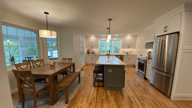 Une cuisine moderne avec un plancher en bois, des meubles blancs, un îlot central et des appareils en acier inoxydable.