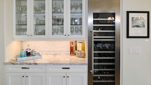 A kitchen with white cabinets, a wine fridge, and a tiled backsplash. - Luxury Waterfront Home (Coronado)