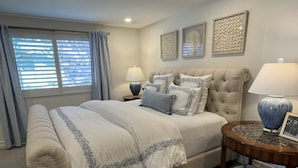 A bedroom with a large bed, two bedside tables, a nightstand, a window with blinds, and a wall with three framed artworks. - Luxury Waterfront Home (Coronado)