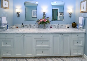 Une salle de bain avec deux lavabos, un vase de fleurs et un grand miroir.