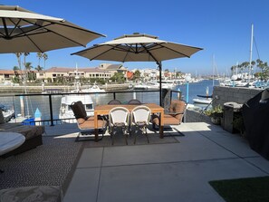 Une terrasse extérieure avec une table et des chaises, entourée de parasols, donnant sur une marina où l’on aperçoit des bateaux et des bâtiments en arrière-plan.