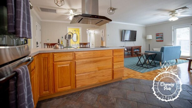 Une cuisine moderne avec des meubles en bois, un îlot central et un four encastré. On y trouve également un coin repas avec un canapé bleu et un téléviseur fixé au mur.