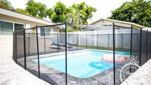Un jardin clôturé avec une piscine, un patio couvert et une vue sur un immeuble résidentiel.