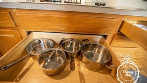 Une cuisine avec des armoires en bois et un plan de travail. On y trouve quatre casseroles et poêles en acier inoxydable sur le plan de travail.