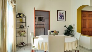 Un'area pranzo con un tavolo rotondo, sedie, un lampadario, una cucina sullo sfondo e una porta con cornice gialla.