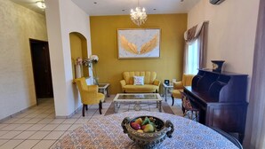 Un soggiorno con un divano giallo, un tavolino da caffè, un pianoforte e un lampadario.