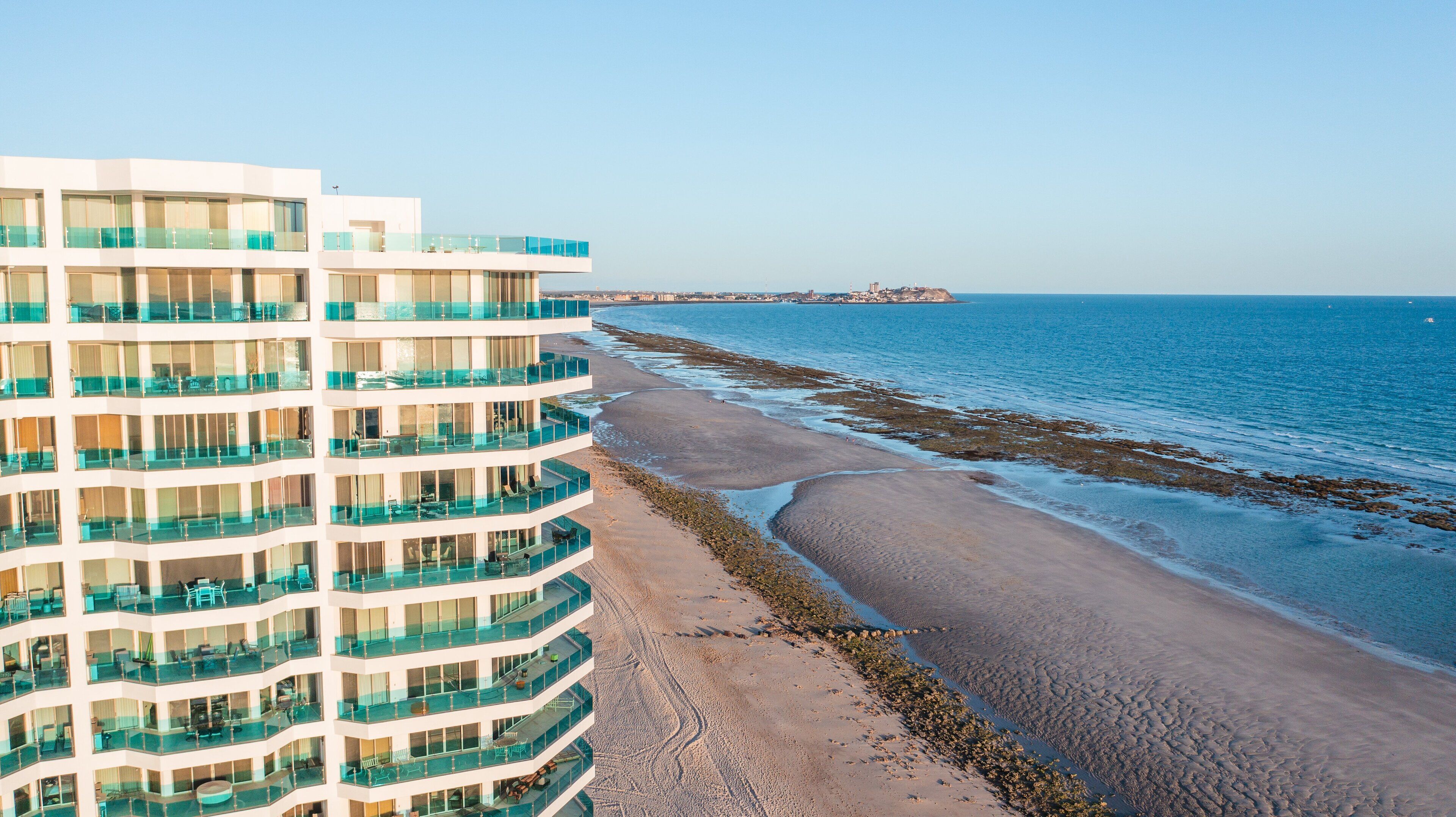Un hôtel à plusieurs étages doté de balcons donnant sur une plage et la mer.