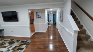 Ein geräumiger Flur mit Holzboden, einer Treppe rechts und einem an der Wand befestigten Flachbildfernseher.
