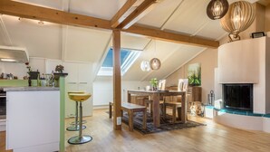 A spacious loft-style kitchen with a dining area, wooden beams, skylights, and a fireplace.