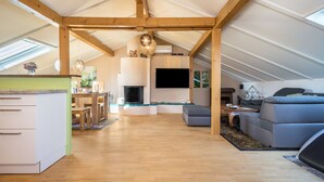 A spacious attic room with a wooden ceiling, a fireplace, a flat-screen TV, and a modern sofa.