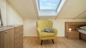 A room with a skylight, a yellow armchair, a bedside table with a lamp, and a wooden dresser.