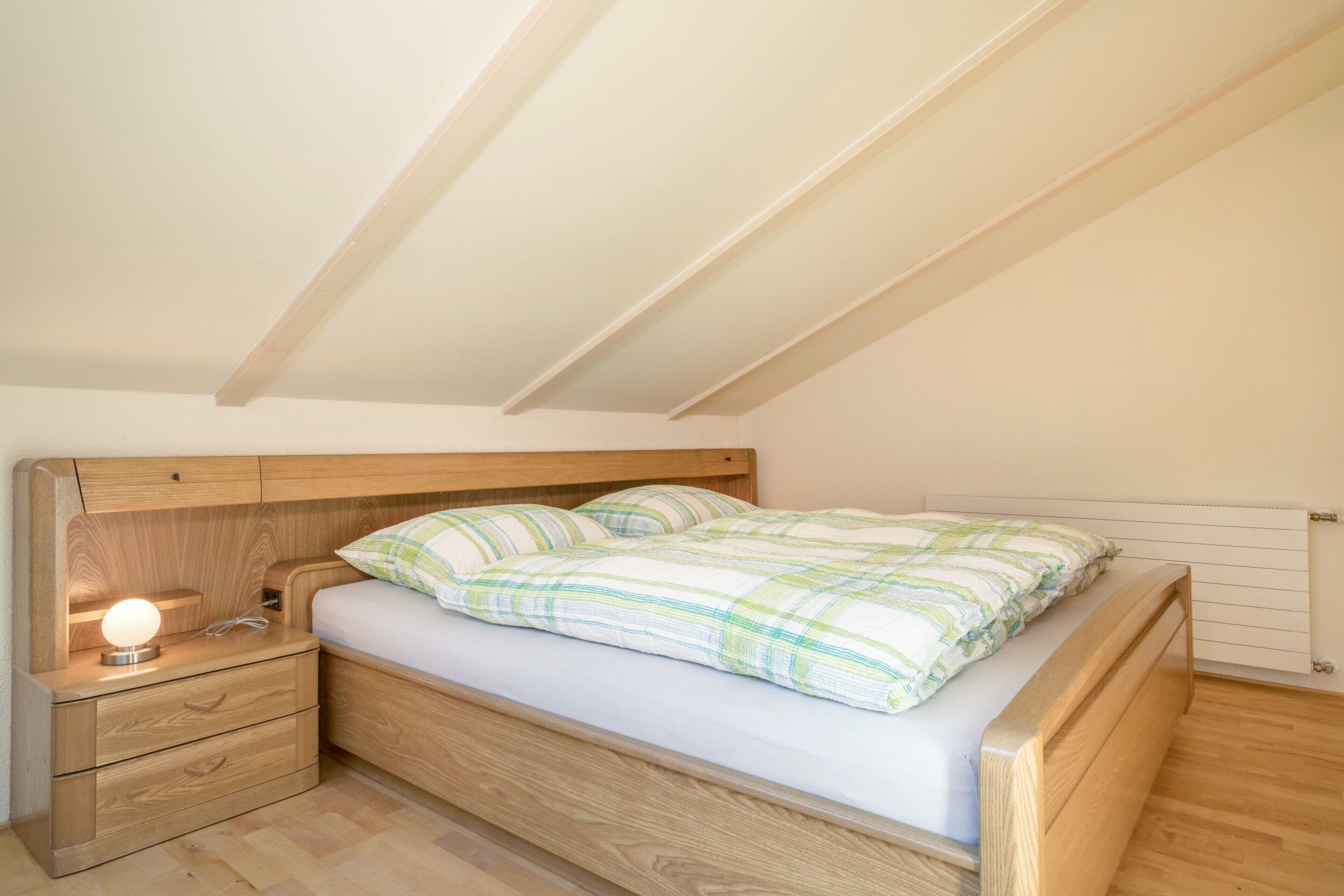 A single bed with a wooden headboard and footboard, a bedside table with a lamp, and a radiator on the wall.
