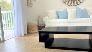 A living room with a white sofa, a black coffee table, and a decorative mirror on the wall. - Bimini Dreams, Steps from the Beach, optional Golf Cart rent (Bailey Town)