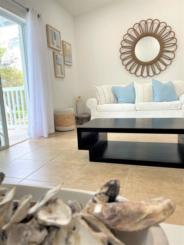 Una sala de estar con un sofá blanco, una mesa de centro negra y un espejo decorativo en la pared.