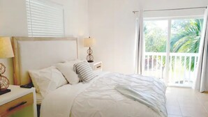 A bedroom with a bed, a nightstand, a lamp, and a view of the outdoors through a sliding glass door. - Bimini Dreams, Steps from the Beach, optional Golf Cart rent (Bailey Town)