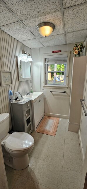 A compact bathroom with a toilet, sink, and window. - Cozy cottage on Pleasant Pond (Warner)