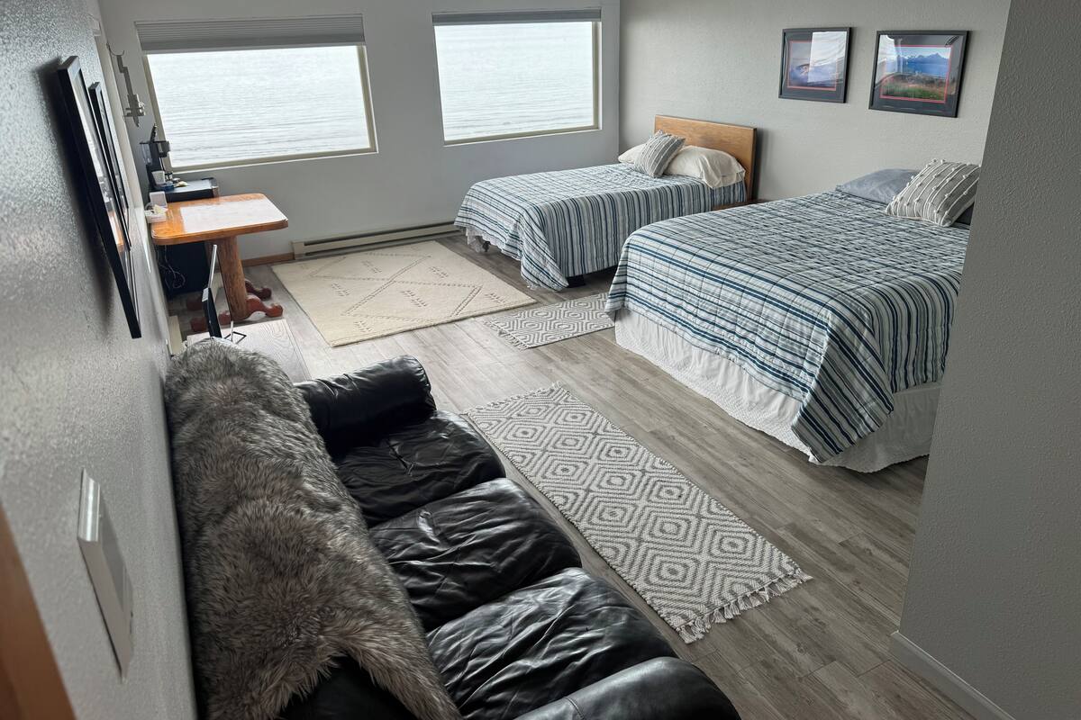 A bedroom with two beds, a desk, and a view of the outdoors.