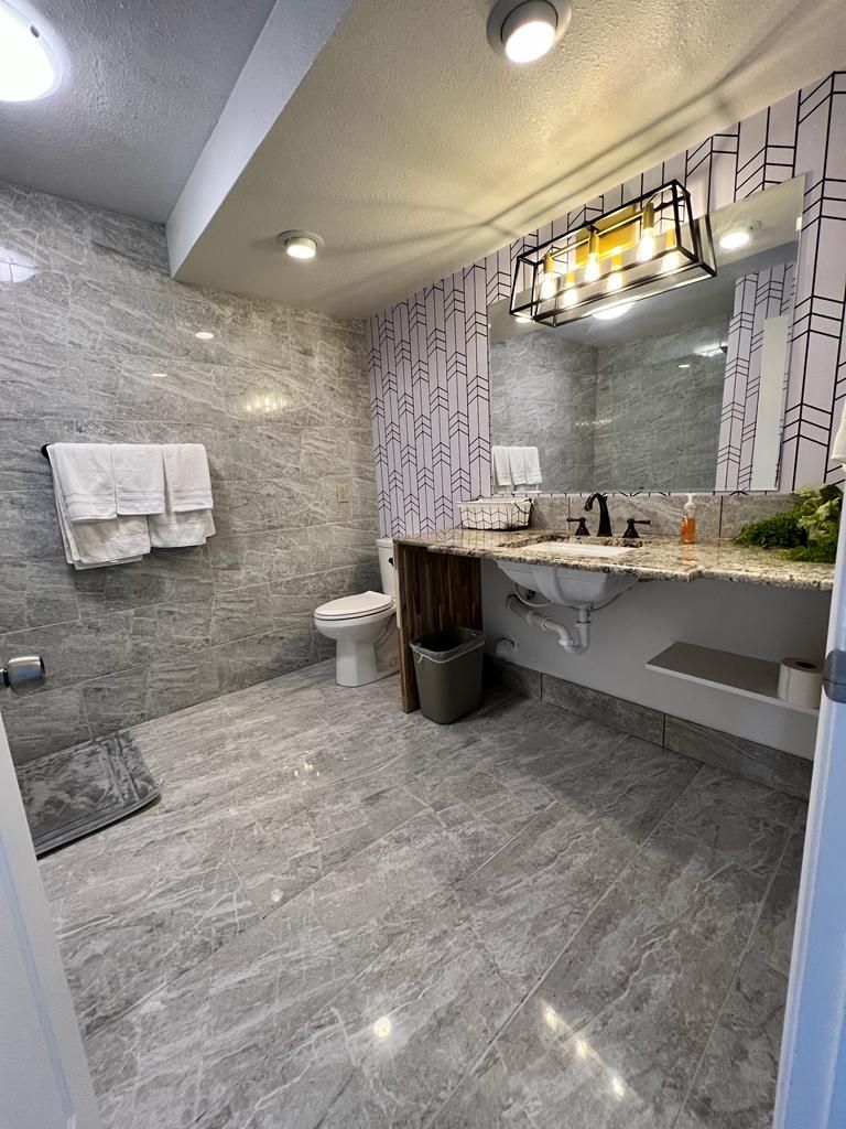 A modern bathroom with a marble floor, a toilet, a sink with a mirror, and a shower area.
