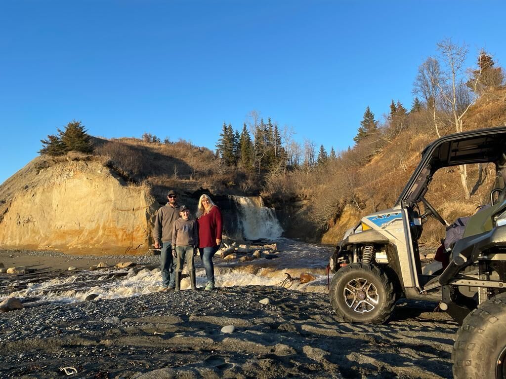 A rocky terrain with a vehicle and two people standing near a waterfall.