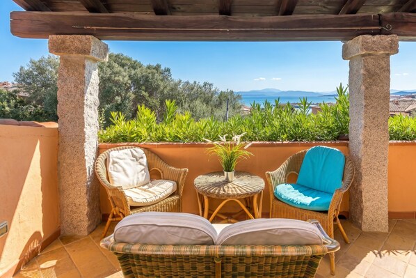 Un espace extérieur abrité, aménagé avec des meubles en osier et offrant une vue sur la mer.
