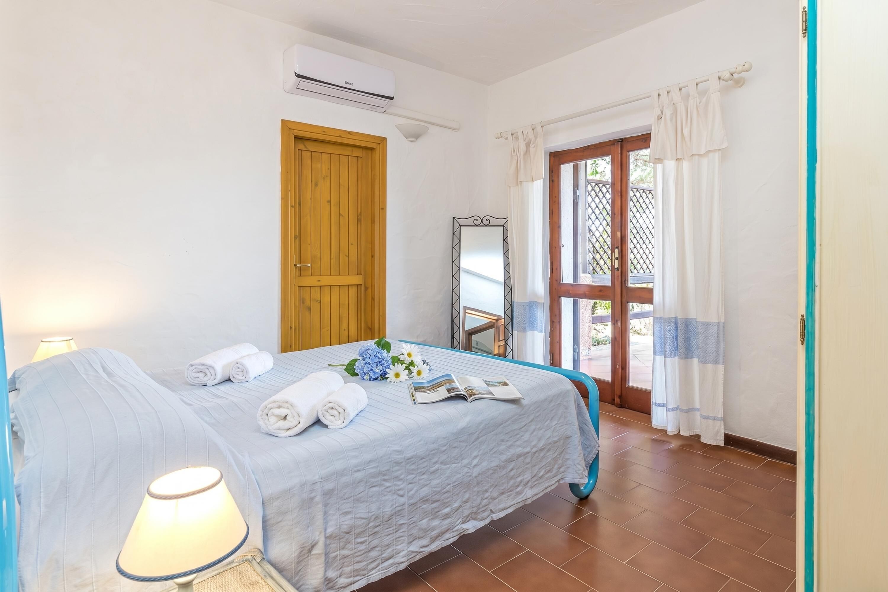 Una camera d'albergo con un letto, una finestra con tende, un condizionatore e una porta.