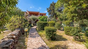 A stone pathway leading to a building with a red-tiled roof, surrounded by well-maintained greenery and a stone wall on one side. - Erica Piano Terra 150m From the Beach, Golfo Aranci, Italy (Golfo Aranci)